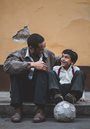 a boy and man sitting on a curb next to a soccer ball